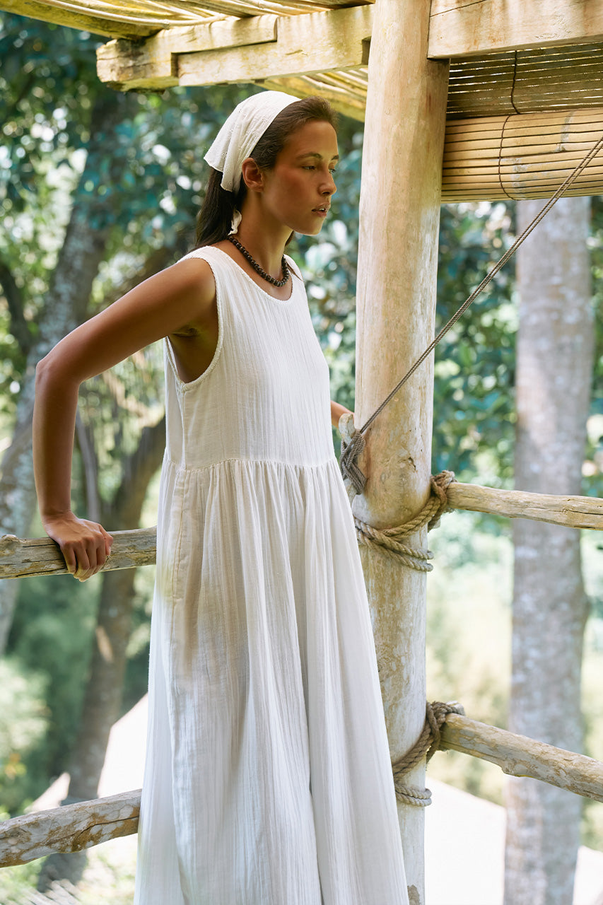 Nadi Dress White — side profile on tropical balcony, white double gauze cotton midi dress showing flowing silhouette, bamboo railing and greenery | Daughters of India