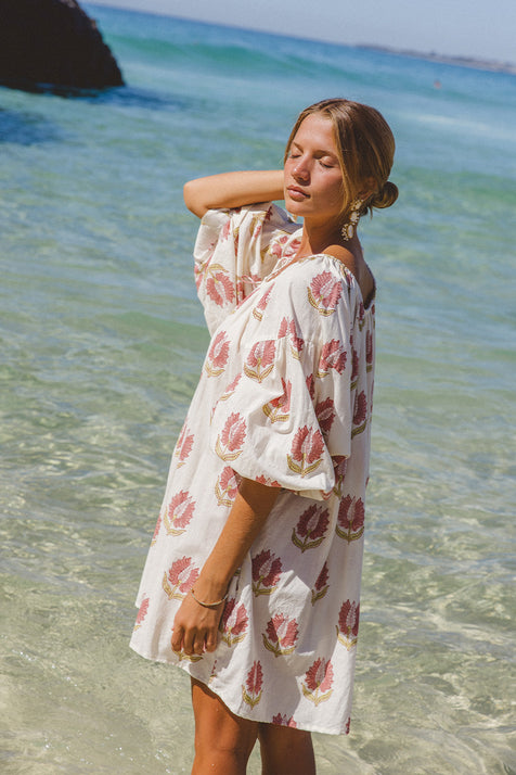 Ria Mini Dress Strawberry Cream — beach lifestyle shot, model wearing strawberry cream floral hand block print cotton mini dress, short hemline with relaxed fit, artisan Jaipur India | Daughters of India